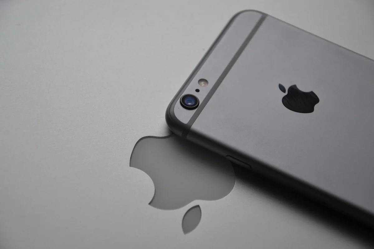 Tył szarego iPhone’a z logo Apple, leżącego na powierzchni z odbiciem logo.