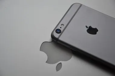 Tył szarego iPhone’a z logo Apple, leżącego na powierzchni z odbiciem logo.
