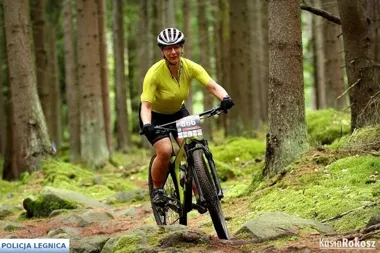 Kobieta w żółtej koszulce i kasku jedzie na rowerze górskim po kamienistej leśnej ścieżce podczas wyścigu MTB.