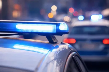 Włączone niebieskie światła na dachu policyjnego radiowozu, w tle rozmyty drugi radiowóz i nocne światła uliczne.